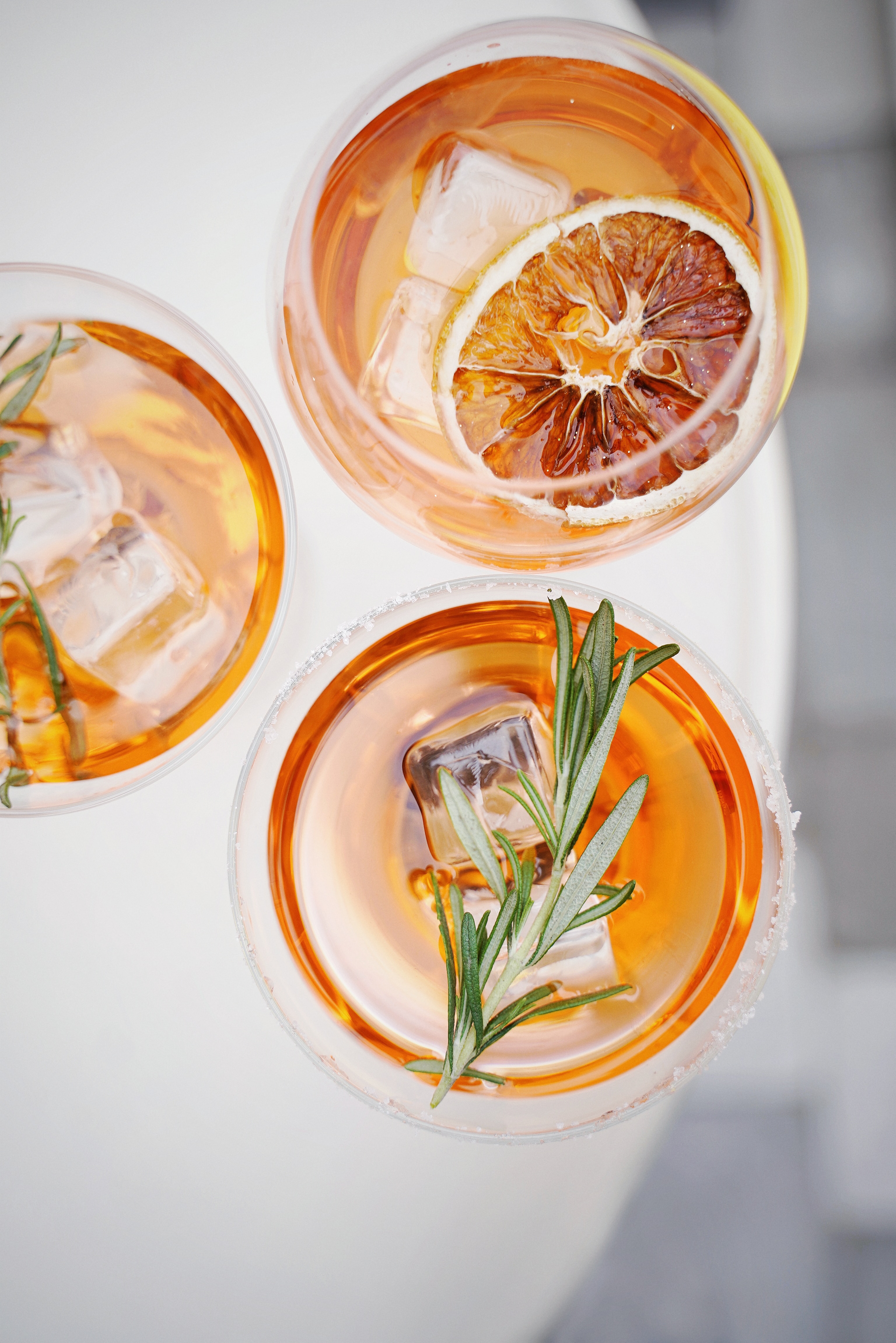 Top view of three cocktails on a surface with a dried blood orange slice and herb garnishes.