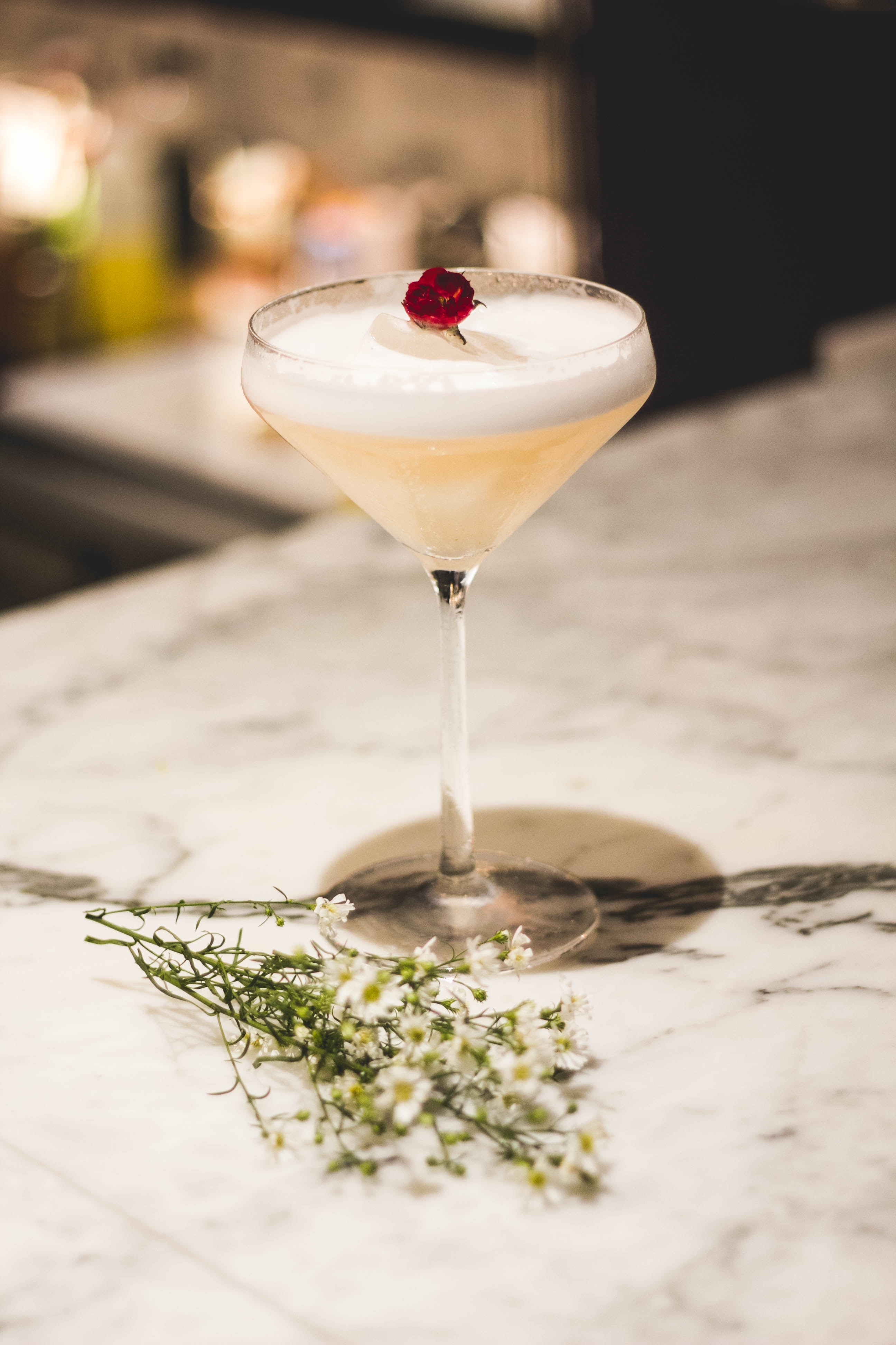 One cocktail on a countertop with flowers on the table and as a garnish.