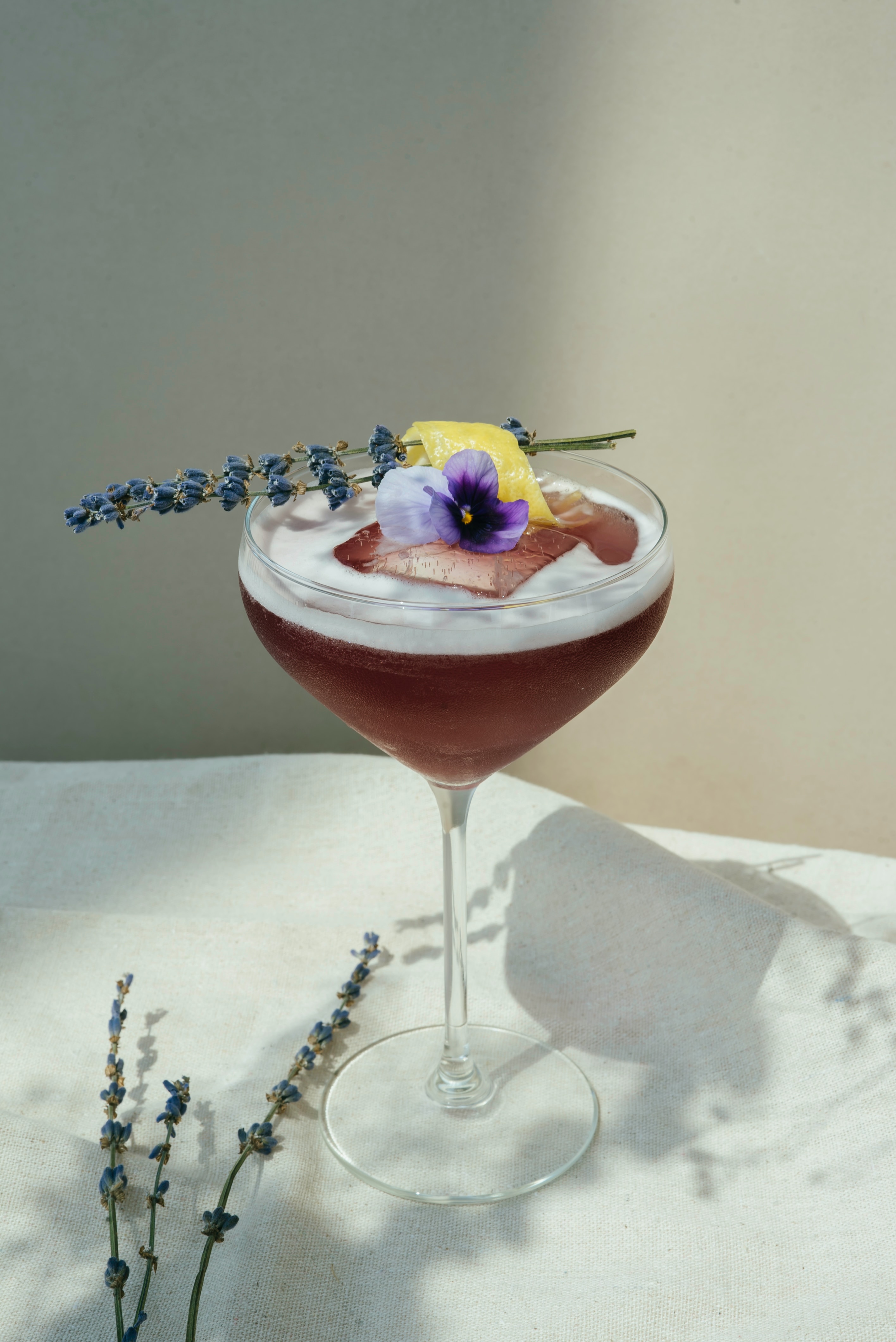 A brown cocktail with flowers and a lemon garnish.