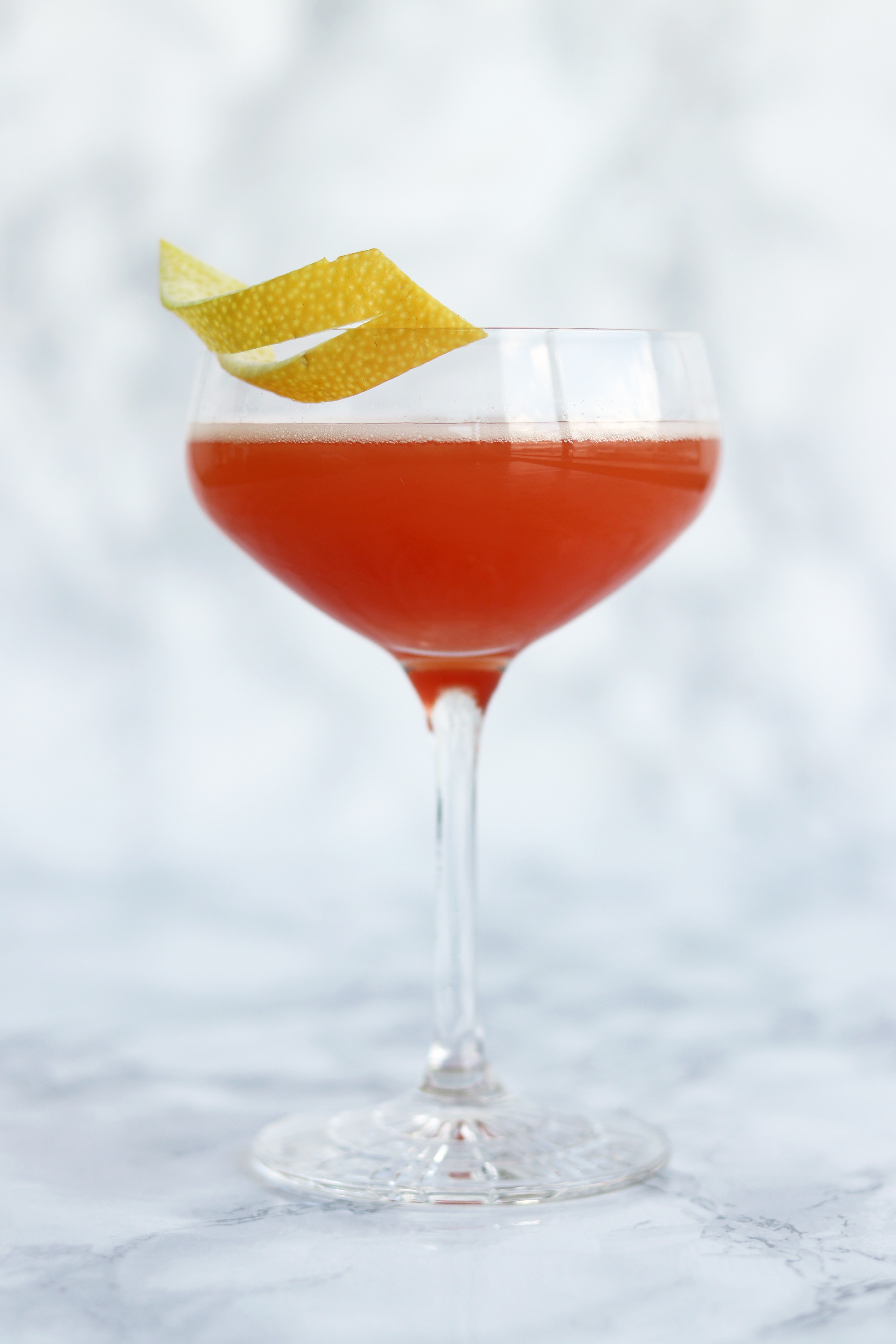 Front view of a red cocktail with a citrus garnish.