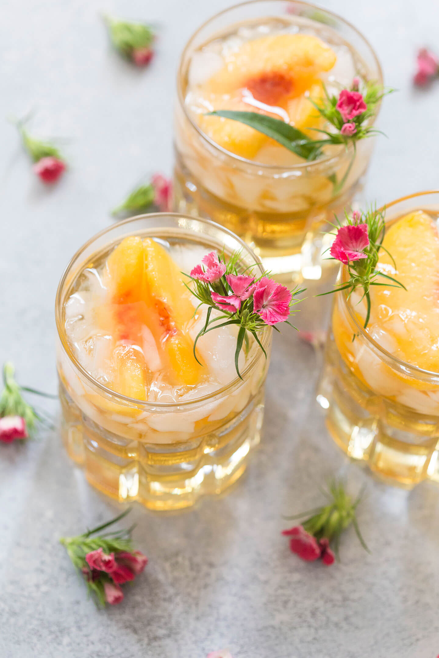 3 peach cocktails on a countertop with small pink flowers.