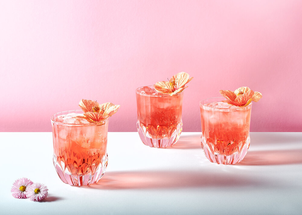 3 cocktails with flowers against a pink background.