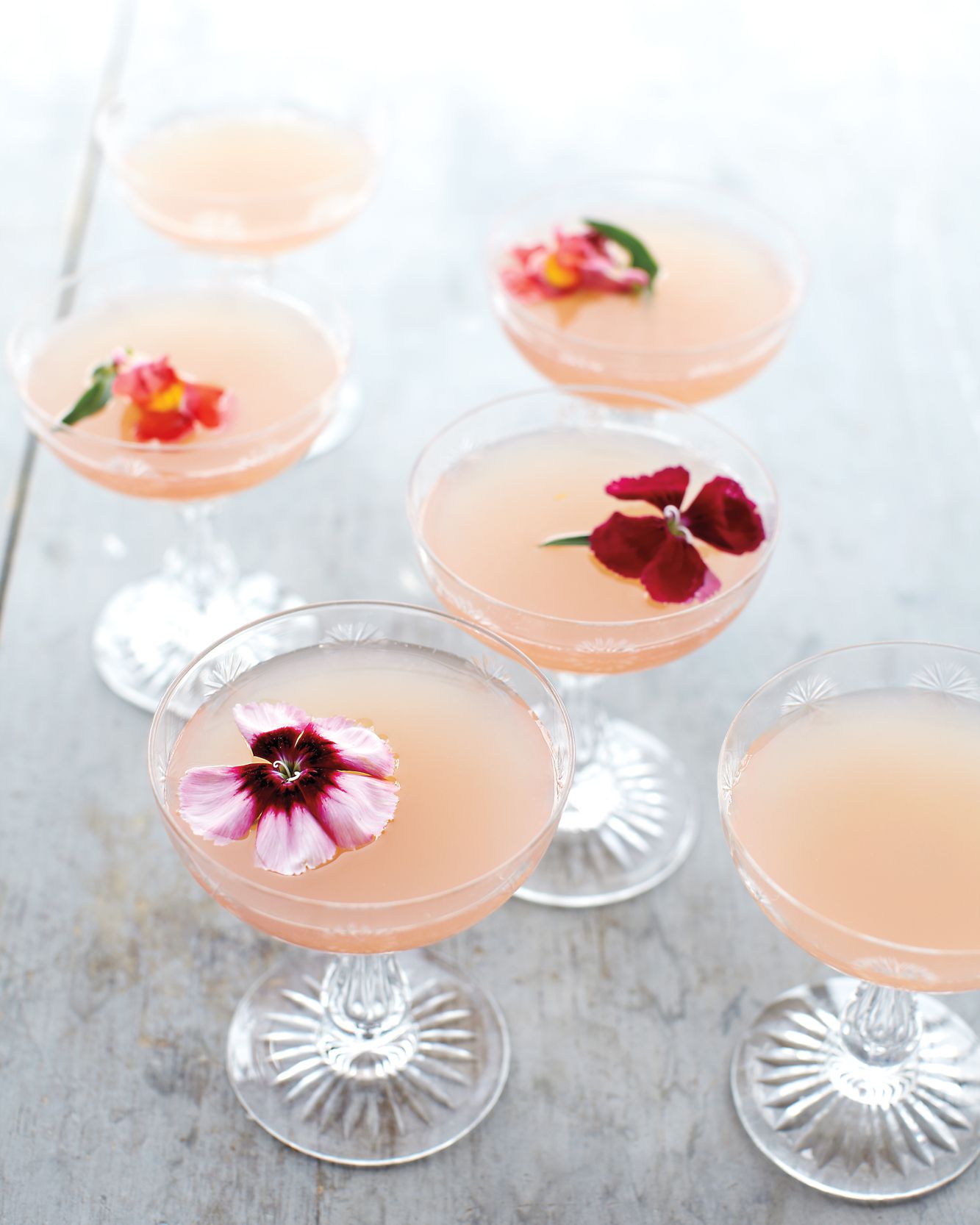 6 drinks on a wooden surface with flowers inside them.