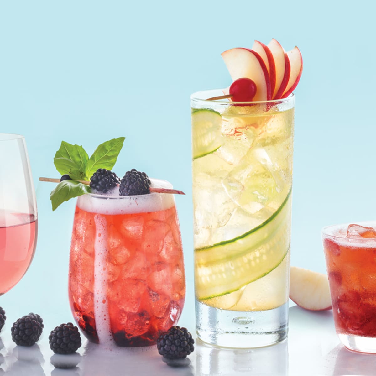 Close up of various cocktails and fruit resting on a surface.